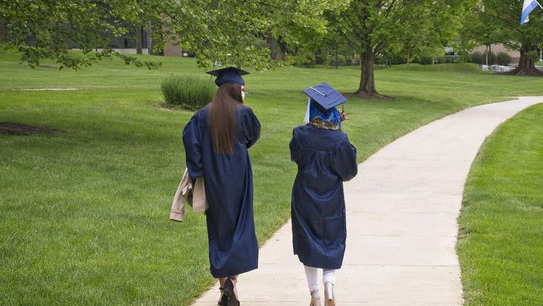 Two students walking while wearing commencement cap and gown.