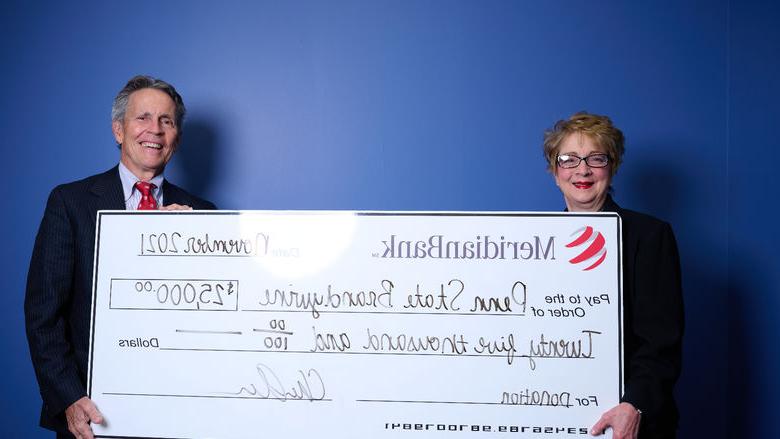 Meridian CEO Chris Annas with 宾州州立大学白兰地酒 总理 Marilyn Wells stand in front of a blue wall holding a large white check. 